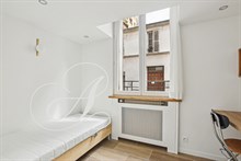 Chambre simple avec vue sur rue pavée dans une location meublée à Paris.